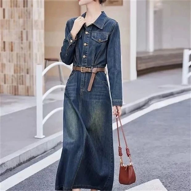 Woman wearing a long denim dress with a brown belt and carrying a matching handbag on a city street.