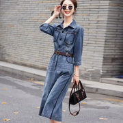 Woman wearing a denim jumpsuit with sunglasses and a handbag on a street.