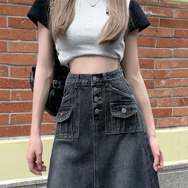 Person wearing a gray crop top and black denim skirt against a brick wall.