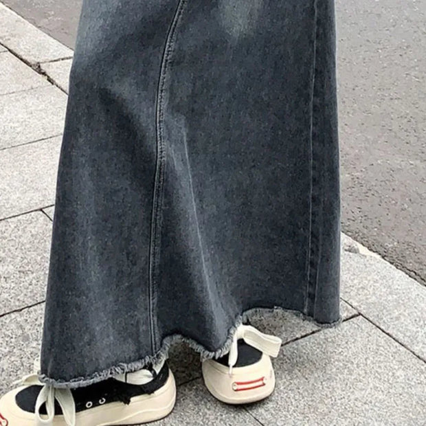 Person wearing a long black denim skirt with sneakers on a pavement.