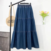 Blue denim skirt on a hanger against a white wall with a bag and flowers in the background.