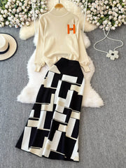 White sweater with orange letter 'H' and black and white patterned pants on a gray surface with decorative elements.