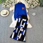 Blue sweater with orange letter 'H' and black and white patterned skirt on a gray surface with flowers and a hat.