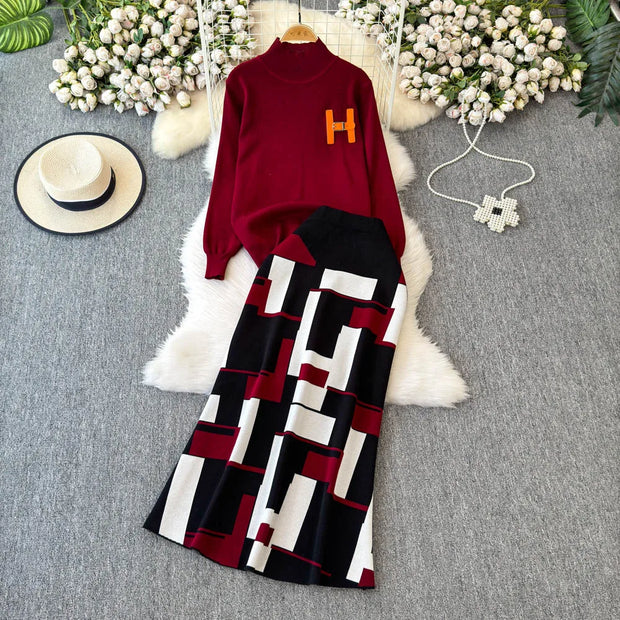 Red sweater with orange letter 'H' and patterned pants on a textured surface with flowers and a hat.