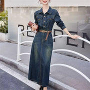 Woman wearing a long denim dress with a belt, standing on a street.