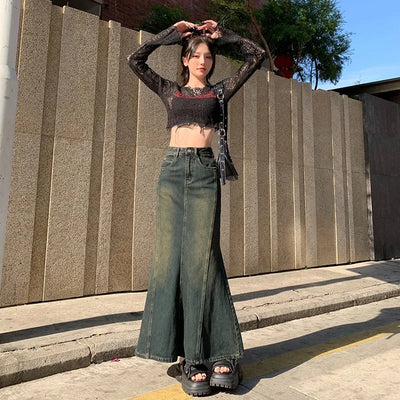 Person wearing a black lace top and green wide-leg jeans standing against a stone wall.