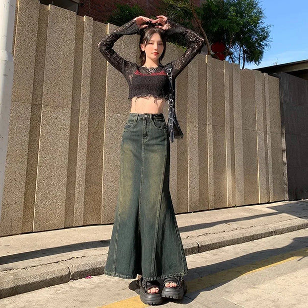 Person wearing a black lace top and green wide-leg jeans standing against a stone wall.