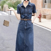 Woman wearing a denim dress holding a beige handbag on a street.
