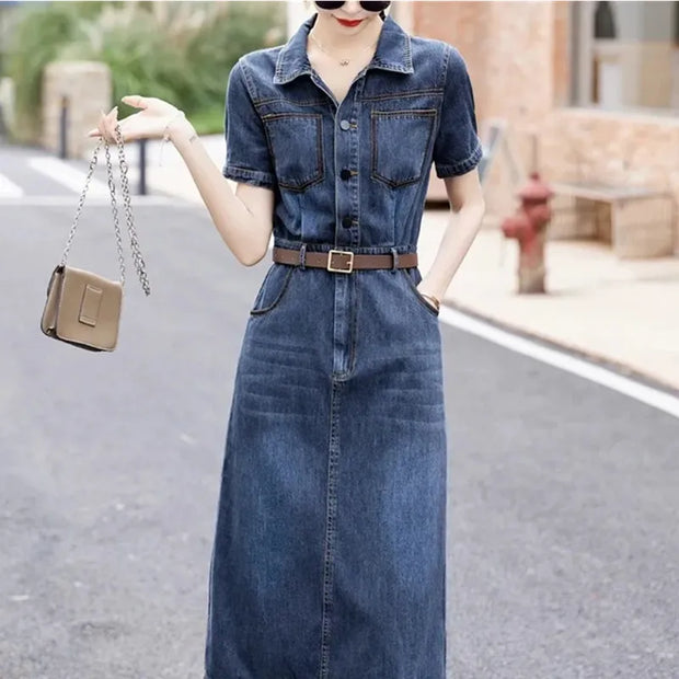 Woman wearing a denim dress holding a beige handbag on a street.