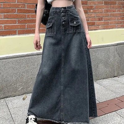 Person wearing a long denim skirt standing on a sidewalk with a brick wall background