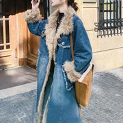 Person wearing a long blue denim coat with fur trim in an urban setting.