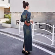 Woman in a long denim dress standing on a street corner with a building in the background.