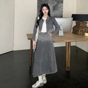 Woman wearing a gray denim outfit standing in a room with a wooden table and lamp.
