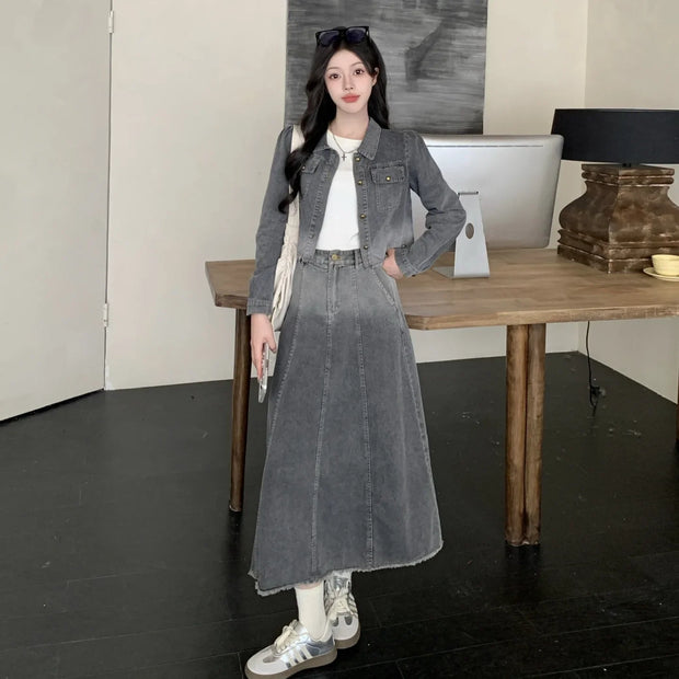 Woman wearing a gray denim outfit standing in a room with a wooden table and lamp.