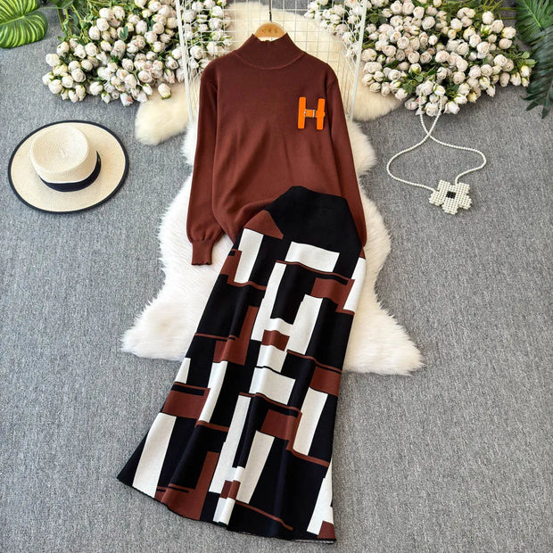 Brown sweater with 'H' logo and patterned skirt on a gray surface with decorative elements.