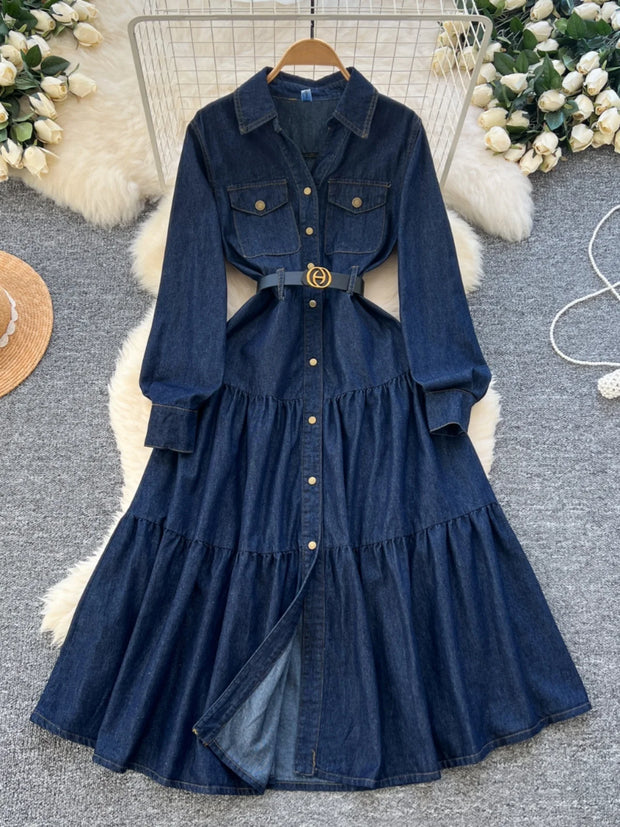Blue denim dress with a belt on a textured surface with decorative elements.